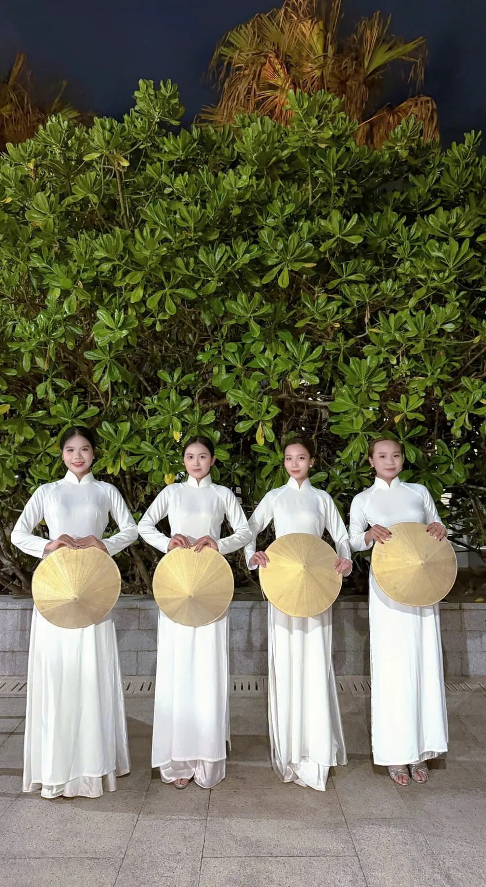 Four dancers in white ao dai holding conical hats