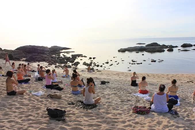 Morning meditation on a sandy beach facing calm sea and rocks