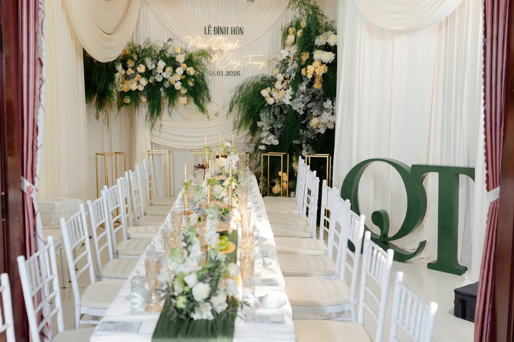 Long banquet table dressed with flowers under white drapes