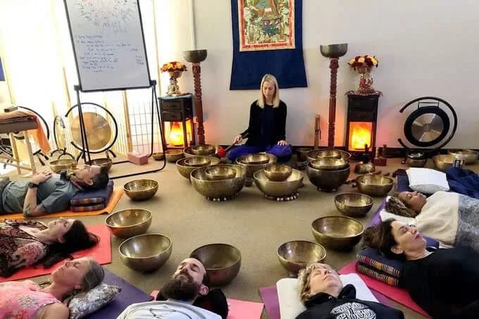 Guests lying on mats among Tibetan singing bowls and gongs during a sound healing session